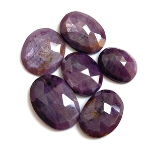 Può includere: Sei gemme ovali sfaccettate in varie tonalità di viola e rosso su sfondo bianco. Le gemme hanno una superficie lucida e riflettente, con motivi interni visibili. L'effetto complessivo è di lusso e bellezza naturale.