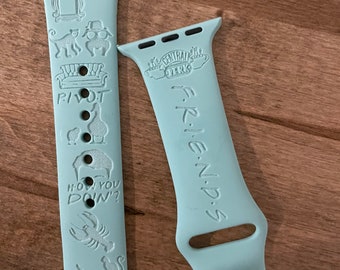 May include: Two light blue Apple Watch bands with Friends themed designs. One band features the Central Perk logo and the word "Friends". The other band features the iconic "Pivot" couch, a lobster, a cat, and the phrase "How you doin'?"