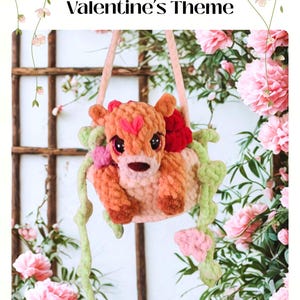 May include: A crocheted fawn-shaped pot with the text "Peek-A-Boo Pot Valentine's Theme" and "Daisy the Fawn." The fawn is peach and brown, with a red heart and flowers. Green vines and pink flowers surround the pot.