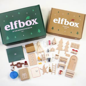 以下が含まれることがあります： 「elfbox」と書かれた2つの箱と、さまざまなミニチュア木製クリスマスデコレーション。箱は緑と茶色です。装飾品には、木、はしご、ベンチ、ドア、小さなセーターが含まれます。「26 TAGE WEIHNACHTSSTREICHE」というテキストが表示されます。