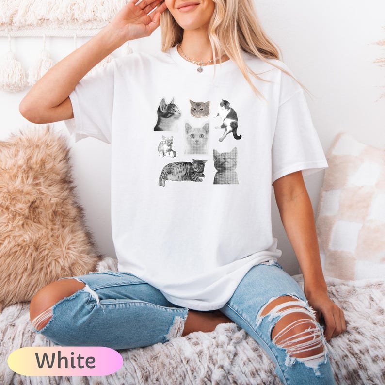 Op de afbeelding: Wit T-shirt met een collage van negen grijswaarden kattenillustraties. De katten worden in verschillende poses en uitdrukkingen afgebeeld. Het woord "White" wordt weergegeven in een roze en gele gradi&euml;nt onderaan de afbeelding.