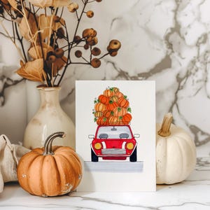 Könnte beinhalten: Aquarellillustration eines roten Autos, beladen mit orangefarbenen Kürbissen. Das Kunstwerk ist vor einem Marmorhintergrund platziert, mit einem kleinen orangefarbenen Kürbis und einem weißen Kürbis im Vordergrund, was ein Herbstthema suggeriert.
