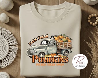 Puede incluir: Sudadera beige con un camión vintage lleno de calabazas. Un esqueleto con sombrero de copa conduce el camión. El texto dice "Farm Fresh Pumpkins, Picked Fresh Daily". Diseño otoñal.