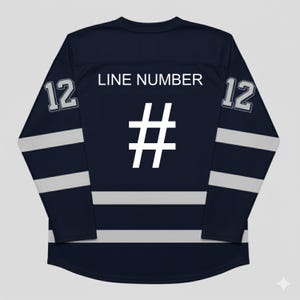 K&ouml;nnte beinhalten: Marineblaues Langarm-Hockeytrikot mit wei&szlig;en Streifen und Akzenten. Das Trikot hat die Nummer 12 auf jedem &Auml;rmel und den Text "LINE NUMBER" &uuml;ber einem gro&szlig;en wei&szlig;en Hashtag-Symbol auf dem R&uuml;cken.
