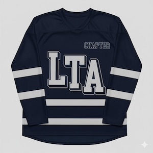 Peut inclure: Maillot de corps bleu marine à manches longues avec des rayures blanches sur les manches et le bas du torse. Le maillot porte le mot "LTA" en grandes lettres blanches sur le devant, avec "CHAPTER" au-dessus. Le maillot a un col en V.