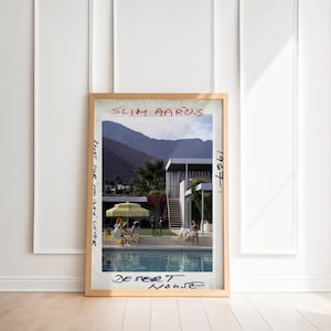 May include: A framed print of a Slim Aarons photograph titled "Desert House." The image depicts a mid-century modern home with a pool, people, and a yellow umbrella. Text includes "Shot for Holiday Cover" and "1967-1."