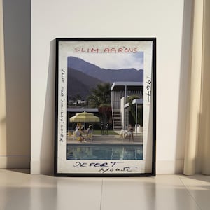 May include: Framed print of a Slim Aarons photograph titled "Desert House" from 1967. The image depicts a mid-century modern home with a pool, mountains in the background, and people relaxing. The text "Shot for Holiday Cover" is also visible.