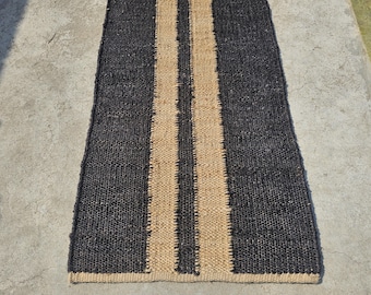 May include: A rectangular jute rug with a central tan stripe flanked by two black stripes. The rug is made of woven fibers and has a textured appearance. The rug is suitable for a hallway or entryway.