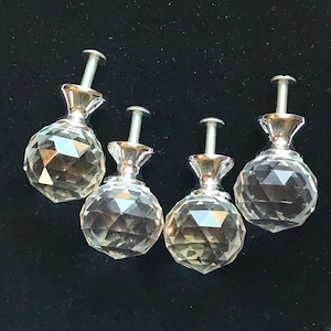 May include: Four clear, faceted glass cabinet knobs with a spherical shape and a polished silver-tone metal base. Each knob features a threaded metal bolt extending from the top, designed for attachment to furniture drawers or cabinet doors.