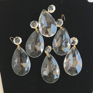 May include: A set of five clear, faceted glass teardrop pendants, each topped with a small hexagonal crystal bead. The pendants are connected by thin gold-toned metal wire loops, creating a dangling arrangement of reflective, transparent glass pieces.