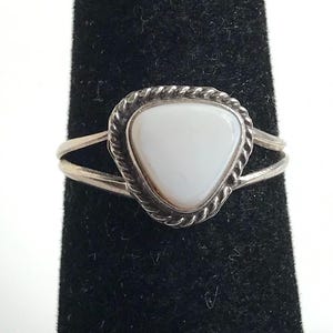 May include: A silver ring with a triangular white stone. The stone is set within a twisted rope-like border. The ring has a split shank design.