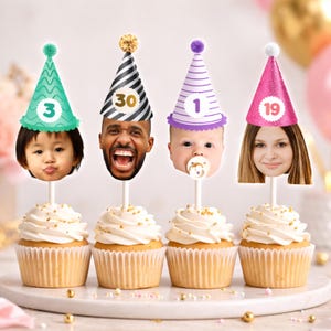 May include: Four cupcakes with personalized face cutouts wearing party hats with numbers 3, 30, 1, and 19. The cupcakes have white icing and gold sprinkles, ideal for a birthday celebration.