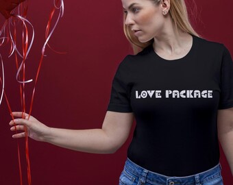 May include: A woman wearing a black t-shirt with the text "LOVE PACKAGE" in white, holding a bouquet of red heart-shaped balloons. The balloons have white ribbons and are against a dark red background.