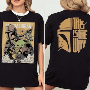 Op de afbeelding: Zwart T-shirt met een afbeelding van The Mandalorian. De voorkant toont een posterachtige afbeelding van de Mandalorian, Grogu en een schip. De achterkant van het shirt heeft een goudkleurige helm en de zin "THIS IS THE WAY."