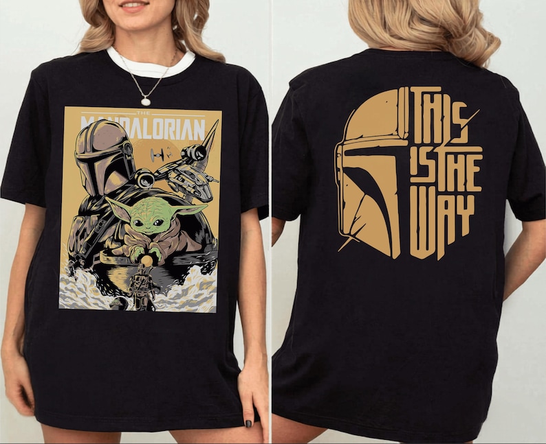 Op de afbeelding: Zwart T-shirt met een afbeelding van The Mandalorian. De voorkant toont een posterachtige afbeelding van de Mandalorian, Grogu en een schip. De achterkant van het shirt heeft een goudkleurige helm en de zin "THIS IS THE WAY."