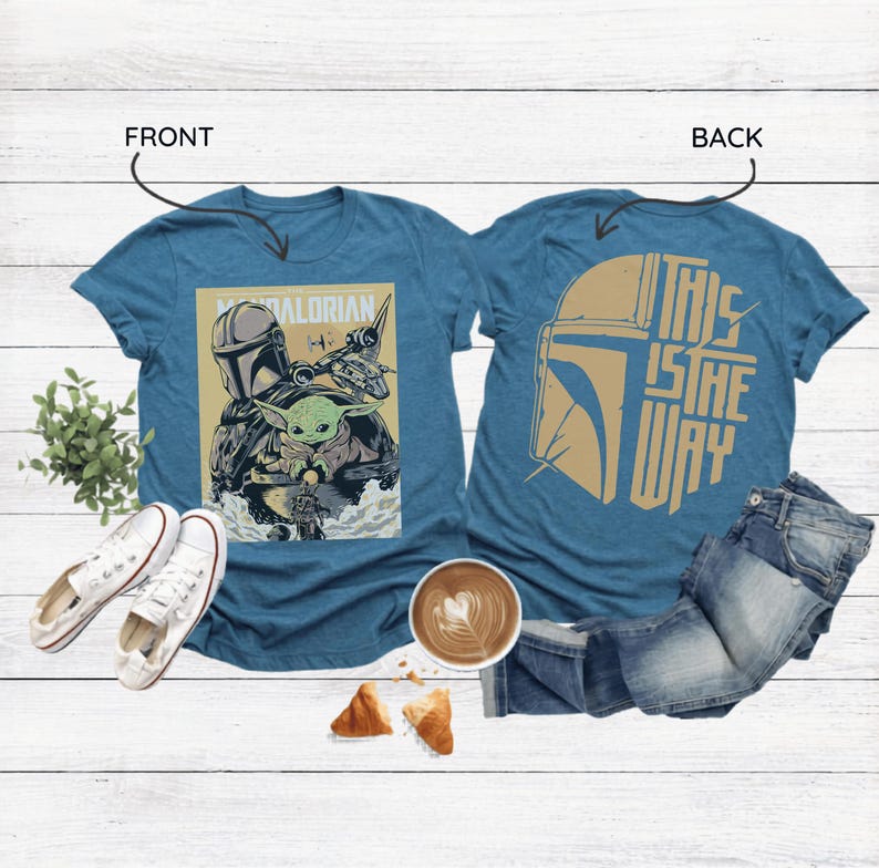 Op de afbeelding: Twee tealkleurige t-shirts met Star Wars-graphics. E&eacute;n toont The Mandalorian en Grogu, de andere heeft een helmdesign en de tekst "THIS IS THE WAY". De shirts worden getoond met witte sneakers, jeans en een koffie.