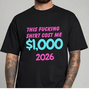 May include: Black t-shirt with the text "THIS FUCKING SHIRT COST ME $1,000 2026" in pink and blue. The shirt is a casual wear item.