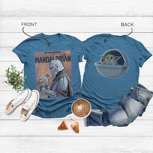 May include: Teal t-shirts featuring Star Wars designs. One shirt displays "The Mandalorian" poster art with the Mandalorian and Grogu. The other shirt shows Grogu in a pod. White sneakers, coffee, and pastries are also in the image.