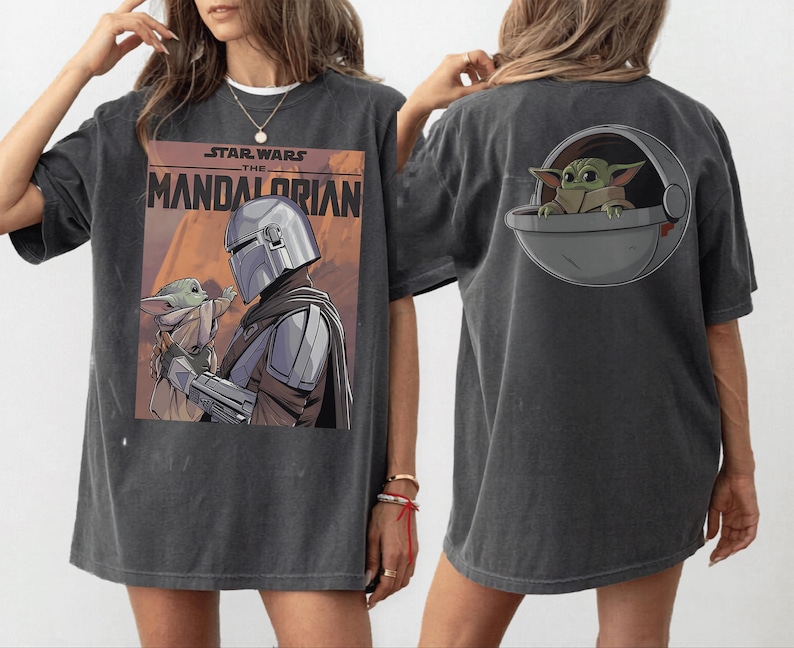 May include: Dark gray t-shirt featuring a graphic from "Star Wars: The Mandalorian." The front displays the show's title and an image of the Mandalorian and Grogu. The back has a Grogu graphic in a pod.