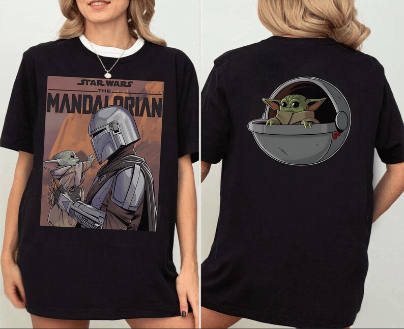 May include: Black t-shirt featuring a graphic from the Star Wars series, "The Mandalorian." The front of the shirt displays the Mandalorian and Grogu. The back of the shirt shows Grogu in a pod. The shirt has a white collar.