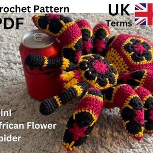 Op de afbeelding: Een gehaakte spin in rood, zwart en geel, met de tekst "Crochet Pattern PDF" en "Mini African Flower Spider". De spin houdt een rode frisdrankblik vast. Het lichaam en de poten van de spin zijn ingewikkeld ontworpen.