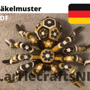 May include: A large, crocheted spider in shades of olive green, mustard yellow, black, and white. The spider has a geometric pattern on its body and legs. The image includes the text "Häkelmuster PDF" and "LarriecraftsNL".