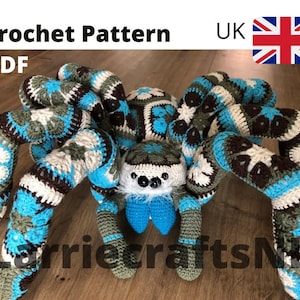 Puede incluir: Una araña grande tejida a ganchillo en tonos de azul, blanco, marrón y verde. La araña tiene ocho patas segmentadas y un cuerpo redondo. El texto "Crochet Pattern PDF" está en la parte superior. La araña es un artículo artesanal hecho a mano.