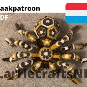 Pode incluir: Uma aranha grande, de crochê, em tons de preto, amarelo e branco, com um padrão geométrico. A aranha tem várias pernas e um corpo detalhado. O texto na imagem diz "Haakpatroon PDF" e "LarriecraftsNL". Uma bandeira do Luxemburgo também está presente.