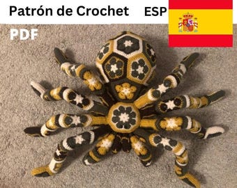 Könnte beinhalten: Eine große, gehäkelte Spinne in Schwarz, Weiß und Gold. Die Spinne hat ein geometrisches Muster auf ihrem Körper und ihren Beinen. Der Text "Patrón de Crochet ESP PDF" befindet sich oben im Bild, mit der spanischen Flagge.