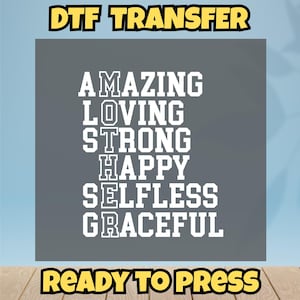 May include: A gray DTF transfer design with the words "AMAZING, LOVING, STRONG, HAPPY, SELFLESS, GRACEFUL" in white, with "DTF TRANSFER" and "READY TO PRESS" in yellow.