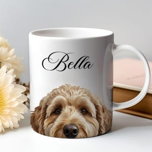 Puede incluir: Taza de cerámica blanca con un retrato de perro. La taza presenta un primer plano de la cara de un perro con pelaje marrón y ojos oscuros. El nombre "Bella" está escrito en cursiva sobre el perro. La taza tiene un asa blanca.