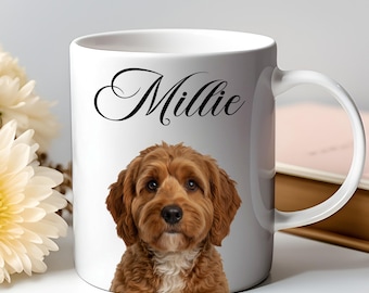 May include: White ceramic mug featuring a portrait of a brown and white dog with the name "Millie" in elegant black script. The mug has a curved handle and is set against a soft background with flowers and a book.