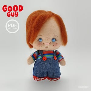 May include: A felt doll with bright orange hair, blue eyes, and freckles, wearing blue denim overalls over a multi-colored striped shirt and red shoes. The text GOOD GUY and PDF PATTERN appear in the upper left corner, with AKEMIFELTS in the bottom right.