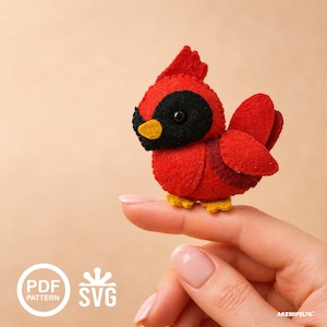 May include: A handmade felt cardinal bird in vibrant red, black, and yellow. The bird has a detailed design with a crest, wings, and a small beak. The bird is perched on a finger. The image also includes the text "PDF PATTERN" and "SVG".
