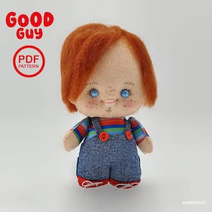 Könnte beinhalten: Eine Filzpuppe mit leuchtend orangefarbenem Haar, blauen Augen und Sommersprossen, die ein gestreiftes Hemd unter einer blauen Jeanslatzhose mit roten Knöpfen und roten Schuhen trägt. Der Text Good Guy und PDF PATTERN steht oben links, AKEMIFELTS unten rechts.