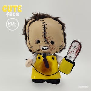 May include: A plush doll featuring a tan mask with dark stitching, brown hair, and a white shirt with a dark tie. The doll wears a yellow apron with brown stains and holds a yellow and silver toy chainsaw with red splatter. Text reads CUTE face PDF PATTERN.