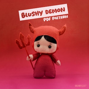 May include: A handmade red felt doll in a devil costume, holding a trident. The doll has black hair and a sad expression. The text "Blushy Demon PDF Pattern" is displayed on a white banner above the doll.