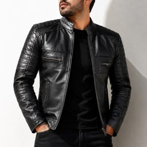 May include: A black leather jacket featuring a mandarin collar, a full-length front zipper, and two horizontal zippered chest pockets. The shoulders and upper sleeves include quilted panel detailing, while the lower sleeves feature ribbed accents.