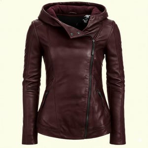 Peut inclure: Veste en cuir bordeaux avec fermeture éclair asymétrique et capuche. La veste a une coupe ajustée, des manches longues et deux poches zippées. La capuche est doublée d'un tissu plus foncé.