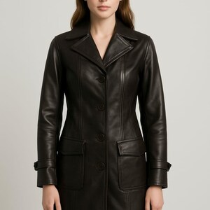 May include: A dark brown leather coat with a notched collar, button closure, and two front pockets. The coat has long sleeves with buttoned cuffs and a tailored fit. The model is wearing the coat.