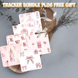Könnte beinhalten: Eine Sammlung von rosa und weißen Tracker-Karten mit Illustrationen von Teddybären, Schleifen, Geschenken und Champagnerflaschen. Die Karten sind auf einem Holztablett mit dekorativen Elementen angeordnet.