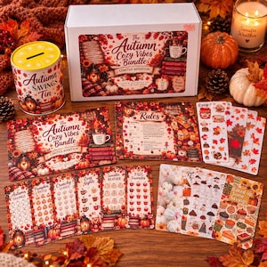 May include: An Autumn Cozy Vibes Bundle set including a savings tin, a large box, rule cards, and multiple tracker sheets featuring fall-themed illustrations of pumpkins, leaves, mugs, and sweaters with text like Autumn Savings and Baked up Some Savings.