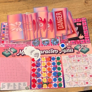 May include: A board game with pink and purple hues, labelled "Character Minis" and "Spill The Tea." The game includes cards, dice, and game pieces. The game board features a word search, a numbered grid, and a winding path.