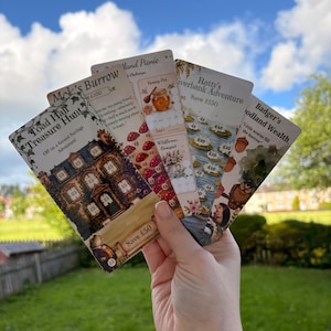 Op de afbeelding: Een set van vier rechthoekige papieren spaarchallenge-kaarten met illustraties in bosthema. De kaarten zijn getiteld Toad Hall Treasure Hunt, Woodland Picnic, Ratty's Riverbank Adventure en Badger's Woodland Wealth, elk met gedrukte valutawaarden.