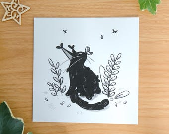 May include: A square white art print featuring a black ink illustration of a cat sitting among plants with a butterfly on its head. The cat has long whiskers and a curved tail. The text by mossyleaf studio is printed at the bottom center.