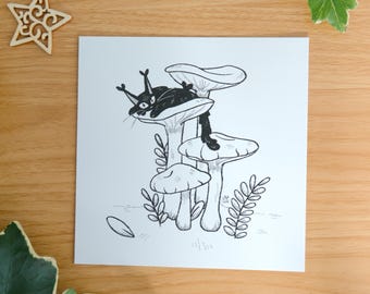 May include: A square white art print featuring a black ink illustration of a cat with tufted ears resting on a cluster of mushrooms. The drawing includes small leafy sprigs and a single fallen petal. The text by mossyleaf studio is printed at the bottom.