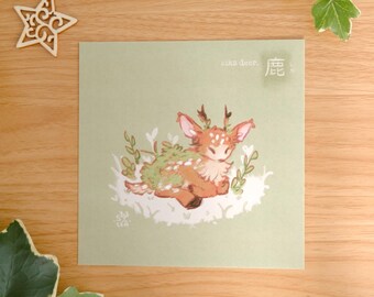 May include: A square art print on light green paper featuring a brown sika deer illustration with white spots and green foliage on its back. The text sika deer and the Japanese character for deer are printed in the top right corner of the print.