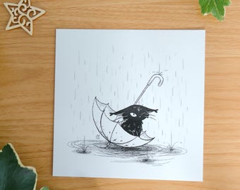 May include: A square art print featuring a black ink illustration of a small creature sitting inside an open umbrella during a rainstorm. The drawing includes vertical lines for rain and a puddle at the base. The text by mossyleaf studio is visible.