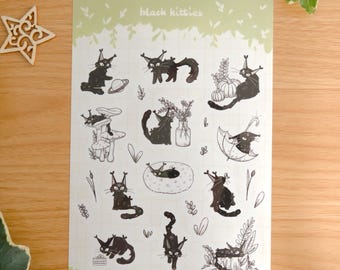 May include: A rectangular sticker sheet with a light green border and the text "black kitties" at the top. The sheet features various black cat illustrations, including cats with pumpkins, mushrooms, an umbrella, a vase, and a planet.
