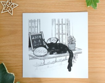 May include: A square art print featuring a black and white ink illustration of a black cat resting on a windowsill next to a loaf of bread, a small potted plant, and a sign with the Japanese text "ようこそ" and a cat face drawing.
